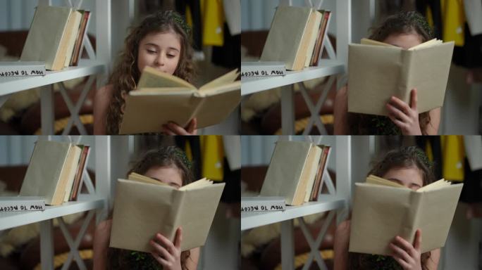 一头长发的可爱的青春期前女孩坐在现代客厅的书柜旁看书。女孩把书放在一边，看着镜头，微笑着。