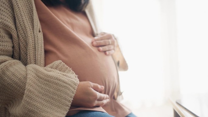 穿着休闲服的成熟孕妇坐在客厅沙发上的特写。触摸你的大肚子，感受宝宝的动作。