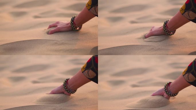印度拉贾斯坦邦斋沙默尔的Khuri沙丘上，印度妇女手抓沙子的特写。游客在沙漠中玩沙子。度假休闲活动概