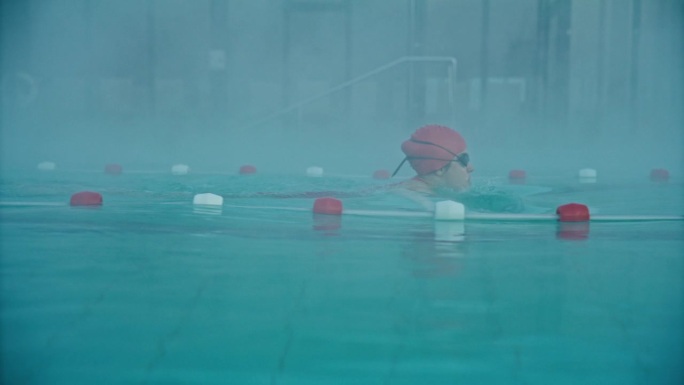 坚定的年轻女游泳运动员在豪华旅游胜地雾池练习蛙泳的侧视图