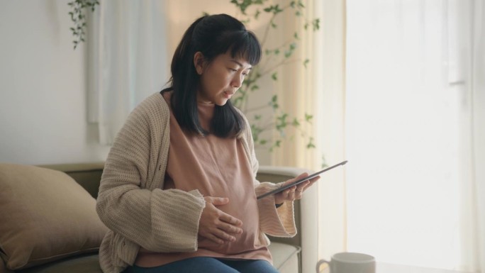 一位亚洲的中国妇女正在看她的孩子在平板电脑上的超声波视频。