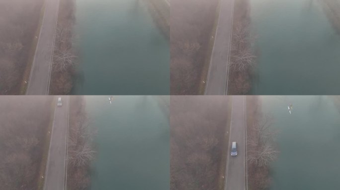 空中:两个人划着他们的小船在雾蒙蒙的河上漂流，一辆汽车在路上驶过