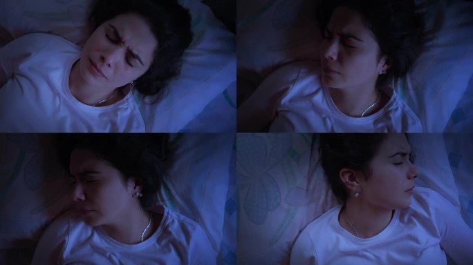 俯视图，一个西班牙裔受打扰的年轻女子晚上躺在床上做恶梦用闪光灯