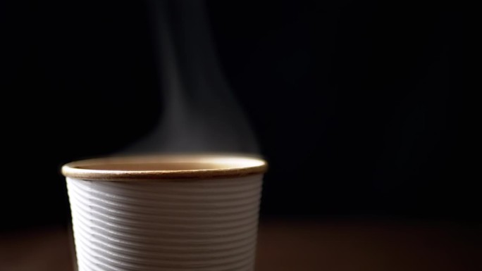 近距离观察，黑色背景上，热咖啡从纸杯里冒出来的热气