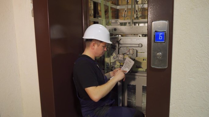 电梯坏了。维修人员在开放的电梯井附近维修电梯设备，并根据设计文件检查各项指标。楼内电梯的技术调整。