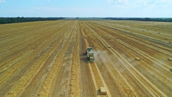 干草打包机拖拉机在田野上行驶，收集稻草并打捆。收获季节的鸟瞰图