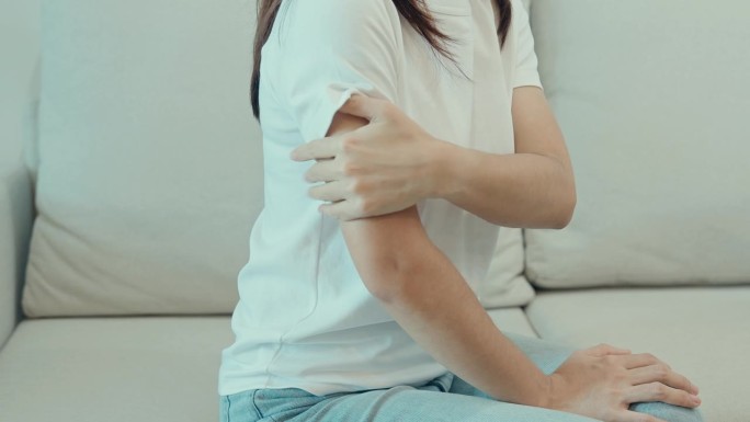 女性在家里坐在沙发上时手臂疼痛，肌肉受伤和疼痛。健康医疗理念
