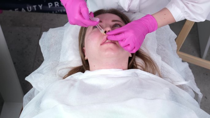 在医疗美容办公室里，一位美容师给一位美丽的年轻女子注射的特写镜头。概念的整容注射，手术和药物。