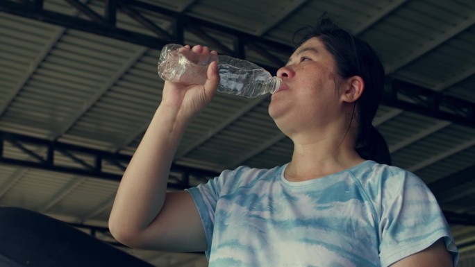 汗流满面，亚洲女人在健身房的跑步机上锻炼，燃烧脂肪减肥，拿着一瓶水，他举起来喝了
