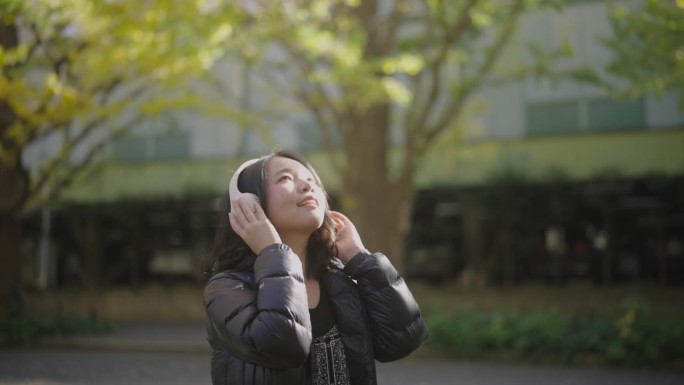 年轻的亚洲女子戴着耳机听音乐。