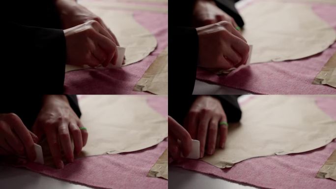 裁缝的手将图案钉在织物上的特写。裁缝用白色的别针把纸样固定在粉红色的纺织品上。