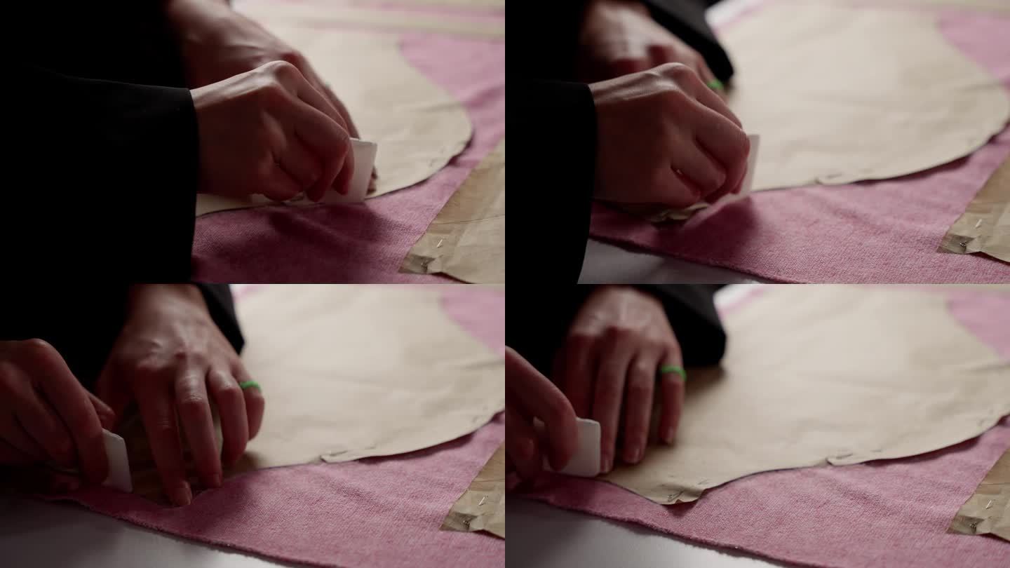 裁缝的手将图案钉在织物上的特写。裁缝用白色的别针把纸样固定在粉红色的纺织品上。