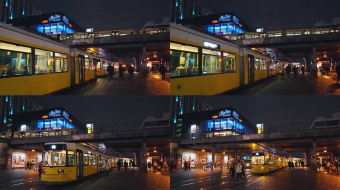 在德国柏林市中心米特区的大型公共广场和交通枢纽亚历山大广场，一群游客在夜间移动着火车和电车