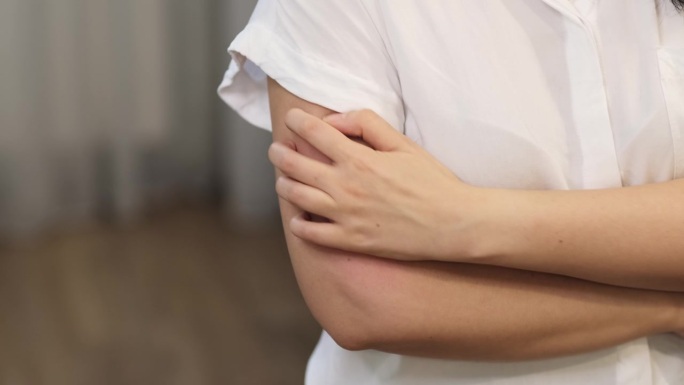 一名年轻的白人女性，由于过敏导致手臂出现红疹和瘙痒，需要抓挠皮肤。这强调了皮肤保健和皮肤病学问题的重
