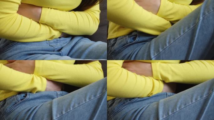 患病的年轻女性遭受月经疼痛的特写。手捏着肚子的女孩坐在沙发上，胃痛或痛经。腹痛和痛经的概念