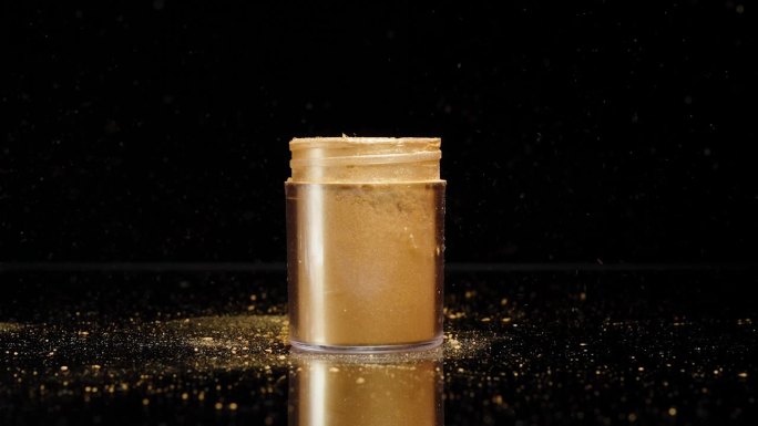 金色的装饰粉从罐子里洒出来。黑色背景的慢动作。