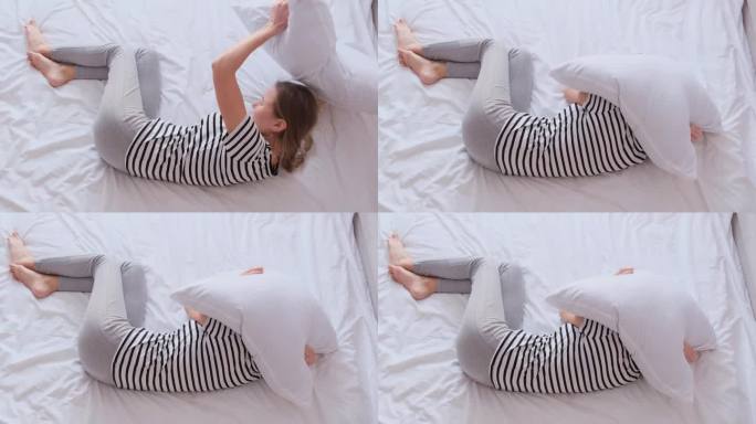 一个失眠的女人躺在床上，用枕头蒙住头。失眠，焦虑或抑郁的概念。
