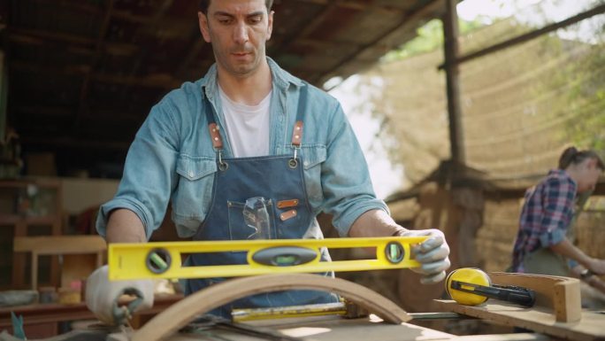 一位男木匠在木工车间用精密水平仪制作新家具。木匠用精密的木器制作家具。木匠和木制品的概念
