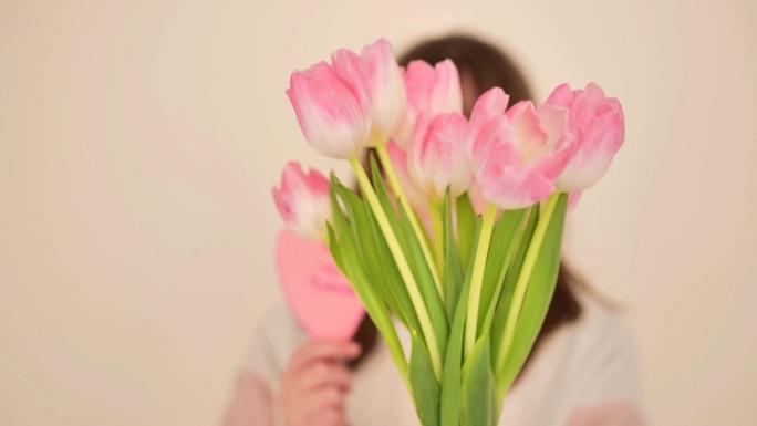 母亲的一天。女儿送给母亲一束粉红色的郁金香和一颗米色背景上的粉红色的心。给妈妈的明信片。