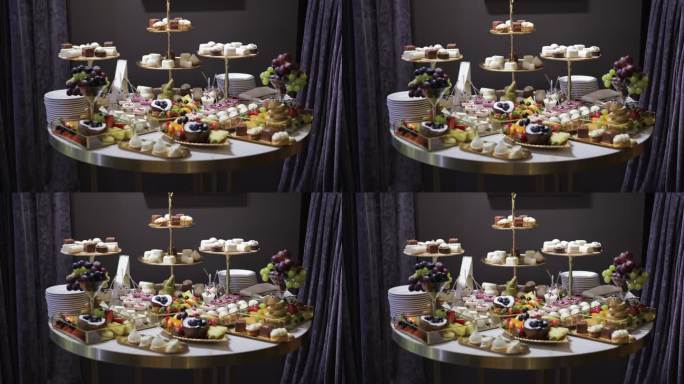 优雅的圆桌上摆放着各式各样的甜点。几种类型的糖果，包括纸杯蛋糕、糕点和水果。三层站在中间，拿着额外的