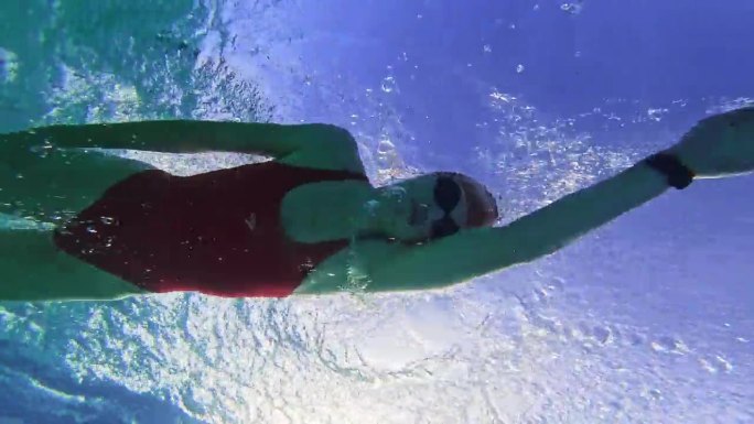 在度假胜地绿松石泳池游泳的坚定的年轻运动女子的水下跟踪拍摄