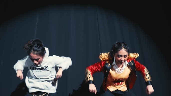 两名年轻的舞者在舞台上表演，灯光引人注目，服装随意。
