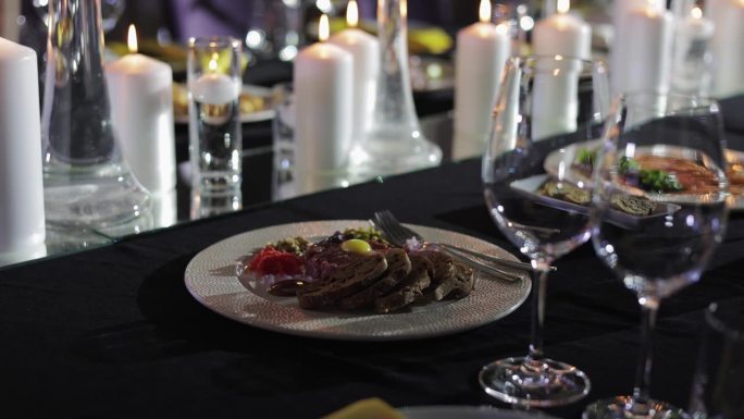 一盘美食突出地展示在前景，各种食材在木桌上。多支白色蜡烛和两个酒杯放置在盘子旁，增添了奢华的气氛。