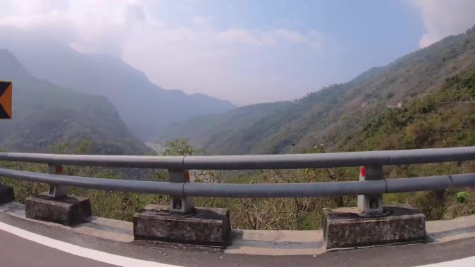 坐在车里哦，在高速公路上的山顶上，看着窗外的荒野景观，周围生长着植被和山脉，远处的河床，阳光，阴天，