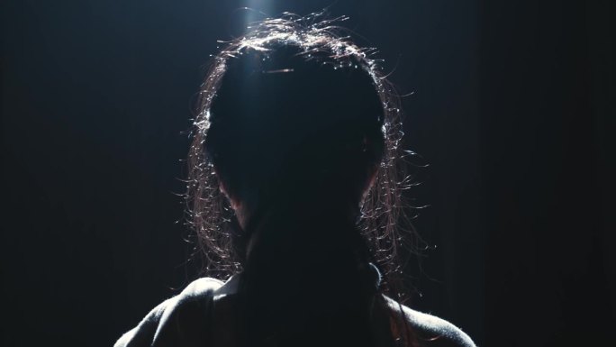 一个人的剪影与背光的头发在黑暗的背景。