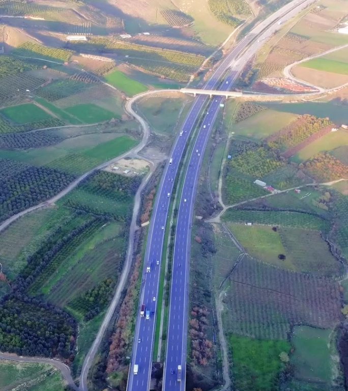 无人机捕捉高速公路上的交通，穿过绿色的田野，蓝天。航拍画面展示了高速公路和乡村。探索高速公路、乡村风
