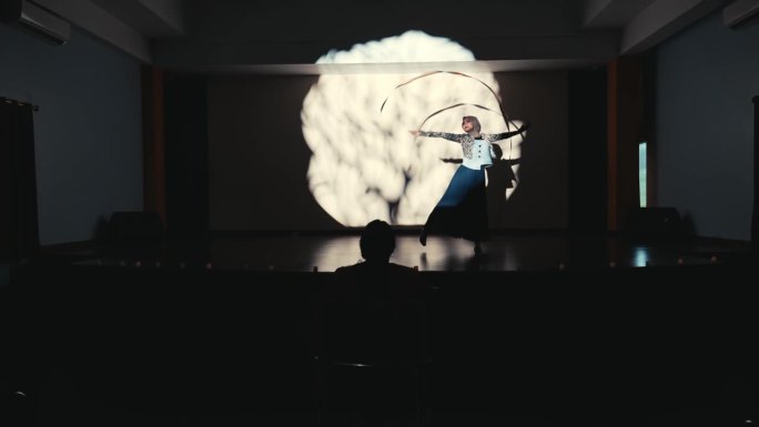 一个人在舞台上的剪影，有戏剧性的灯光，背景是一个投影的大脑图。