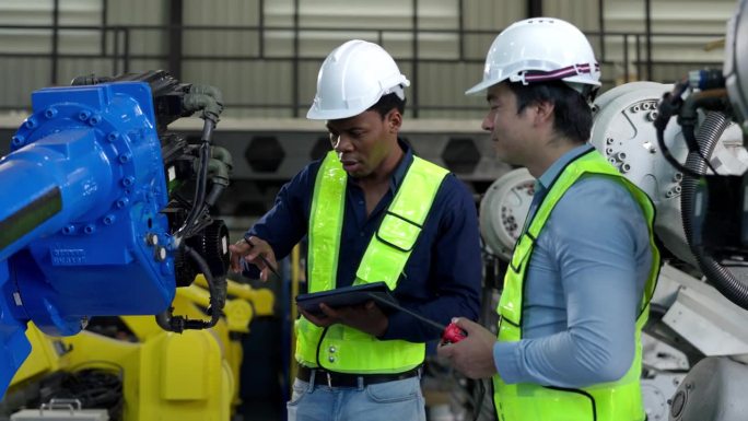 非裔美国工程师、白人技术员在焊接工厂用平板电脑检查机器人机械臂