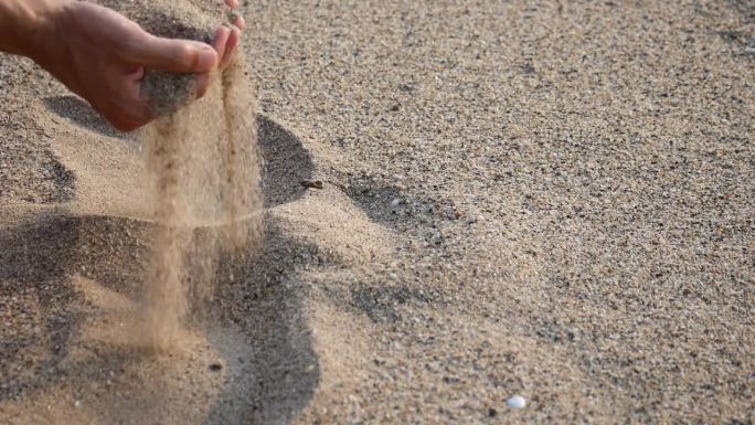 近距离的手释放掉落的沙子。沙子流过双手拍打着海洋