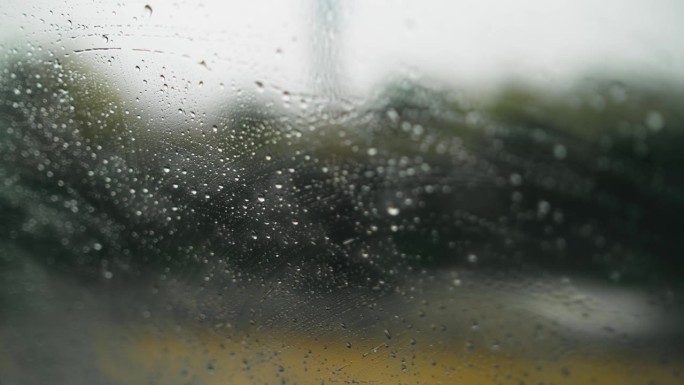 汽车在雨中行驶，侧视图不清晰，雨滴落在窗户上，背景模糊