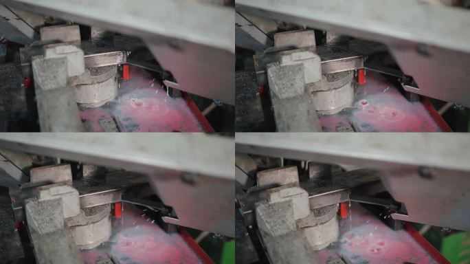 长锯在水冷系统下切割金属板的特写镜头，切割机下的水滴和一些金属残留物。工件金属生产和钢铁工业