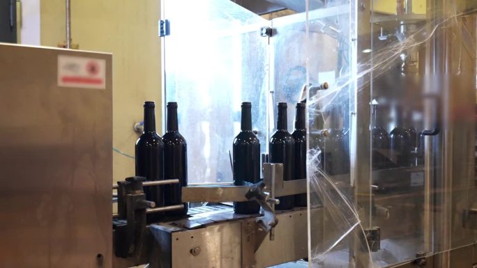 红酒酒瓶在传送带上移动，自动贴标是红酒生产线的最新步骤。装瓶输送机及制造理念