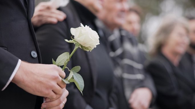 手，玫瑰和一个人在墓地的葬礼上，在追悼会上哀悼失去的亲人。死亡、鲜花和一个穿着西装的成年人在人群中的