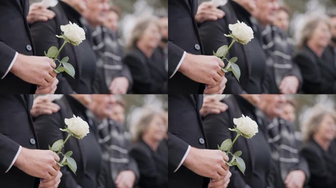 手，玫瑰和一个人在墓地的葬礼上，在追悼会上哀悼失去的亲人。死亡、鲜花和一个穿着西装的成年人在人群中的
