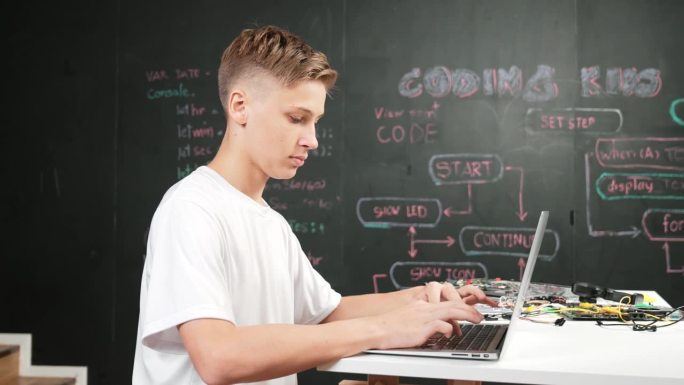 聪明的青少年在桌子上用设备编码或编程系统。启迪