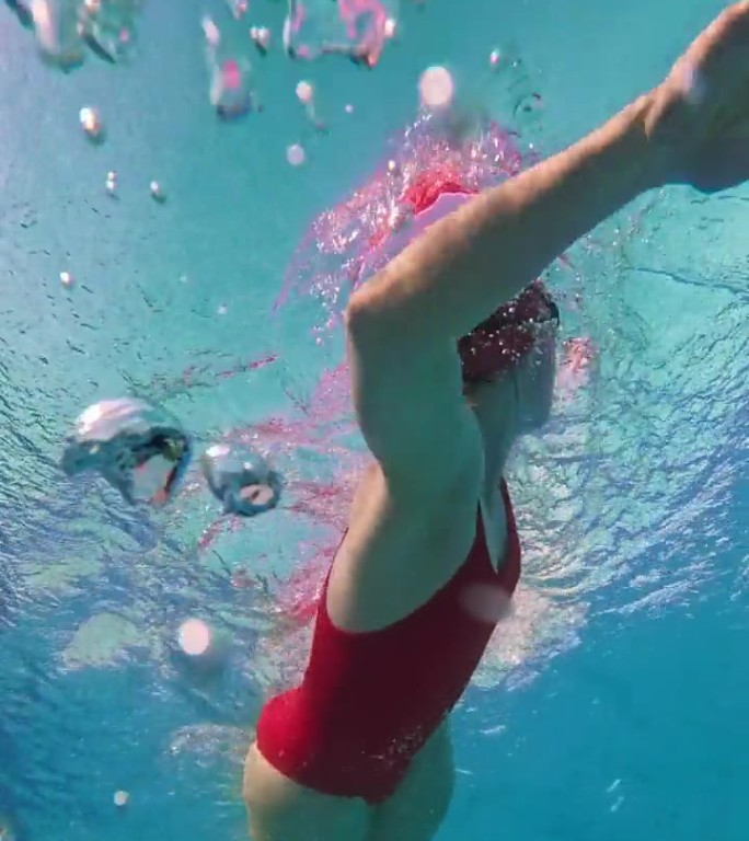 在阳光明媚的日子里，坚定的女子在泳池里练习自由泳的低角度水下镜头