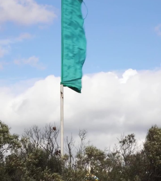 蓝天背景上，蓝色的旗帜在强风中展开。4K垂直视频
