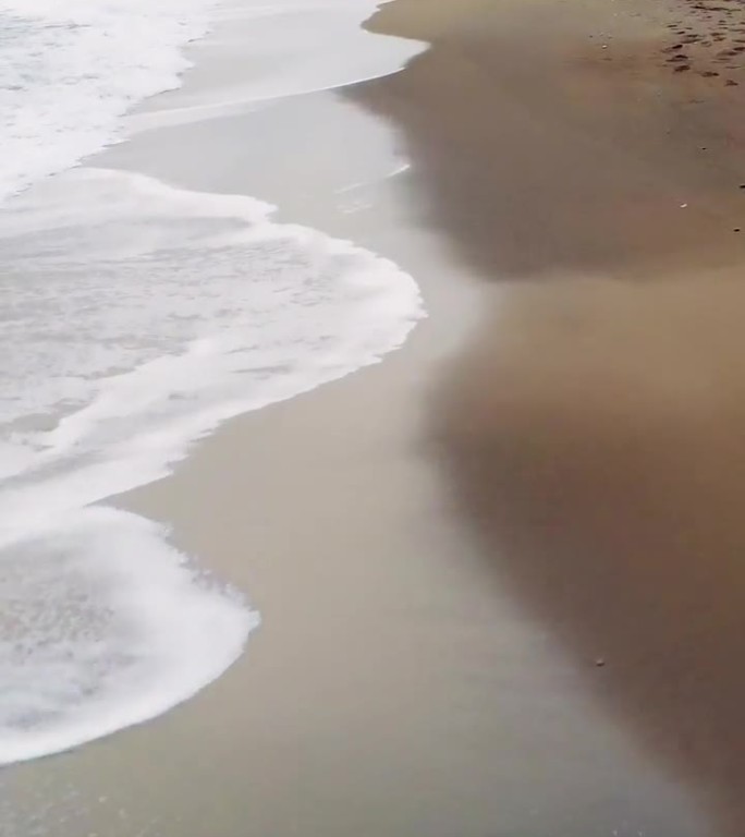 低空无人机沿着沙滩的冲浪线飞行。海岸线一直延伸到地平线，海浪拍打着海岸。在这宁静的景色中探索海洋和海