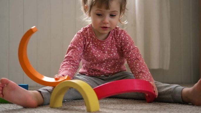 小女孩在家里、幼儿园或托儿所玩玩具。宝宝孩子玩玩具立方体和木头拼图，金字塔坐在地板上。快乐学前教育室