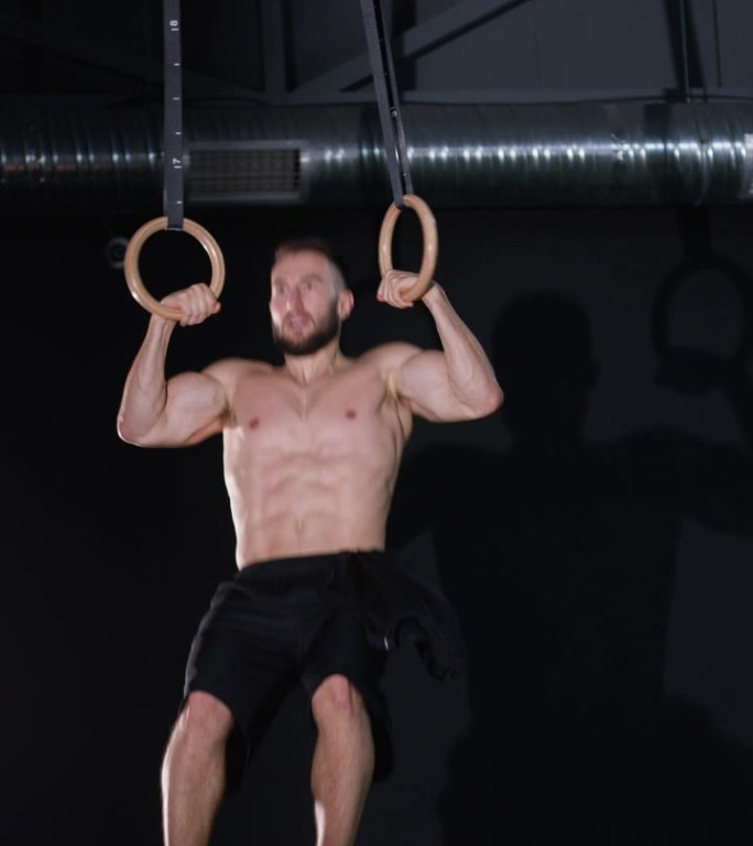 垂直视频。一名男性健美运动员或锻炼者正在健身房的圆环上锻炼