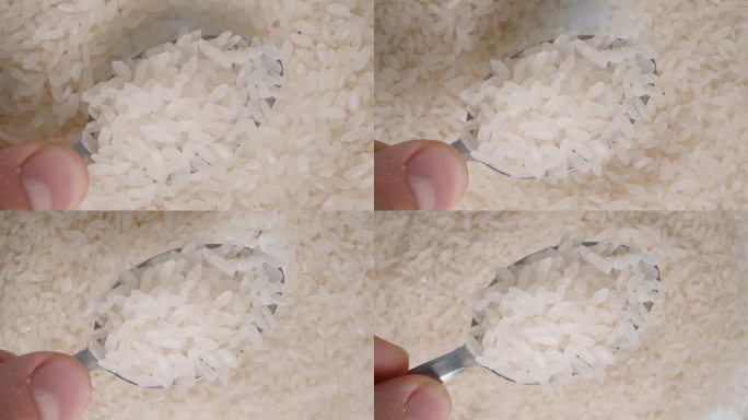 一只手向上举起盛有白米粒的勺子的特写，背景是下面旋转的大米。