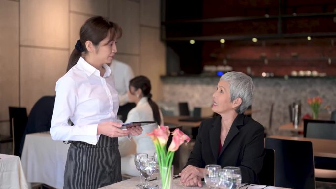 现代待客之道:亚洲见习女服务员接受顾客的数字平板订单