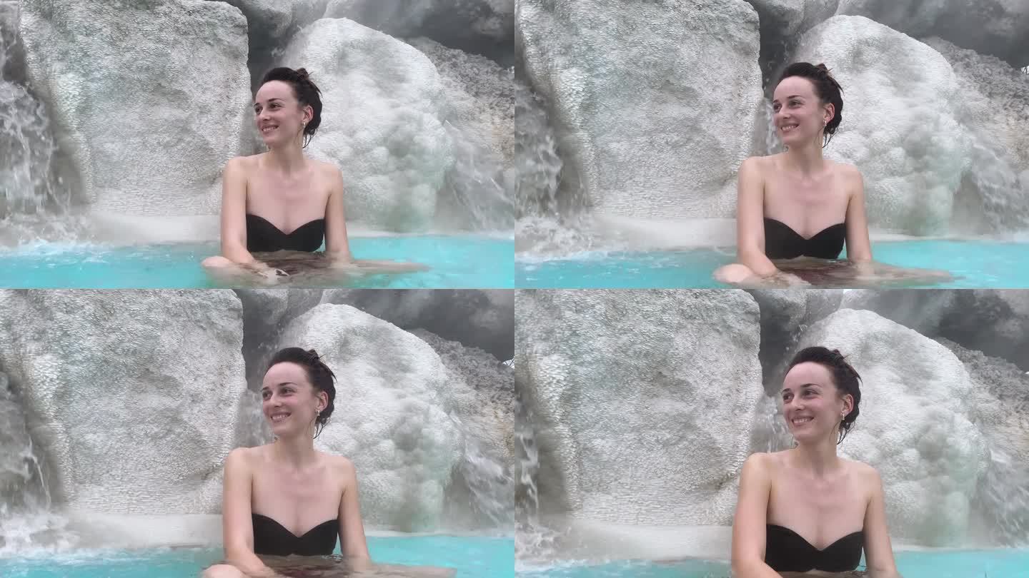 美女坐在瀑布下的温泉池的石头上的肖像，女性在地热温泉中放松，硫磺蒸汽，温泉浴对人体的治疗特性，身心放