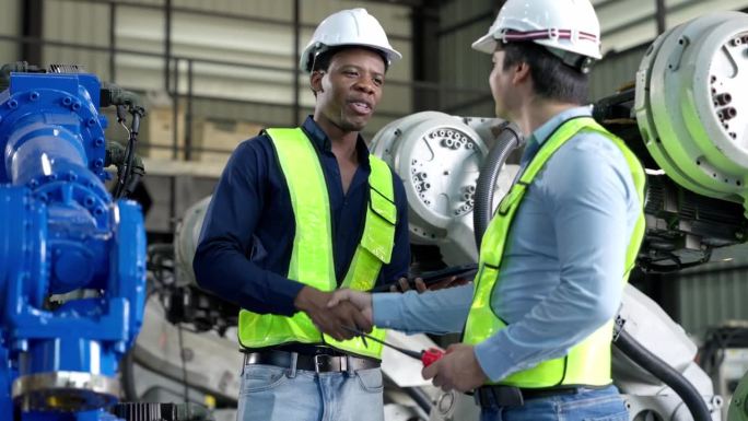 非裔美国工程师，在焊接机器人机械臂工厂拿着平板和握手的技术员