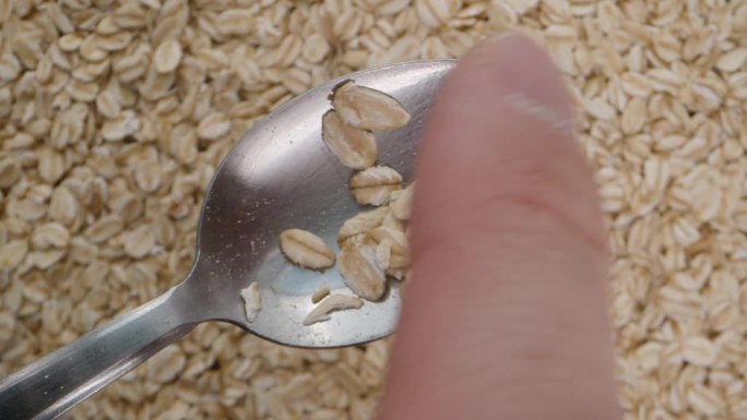 我用手指把勺子上的燕麦片抖掉。以燕麦为背景的特写。
