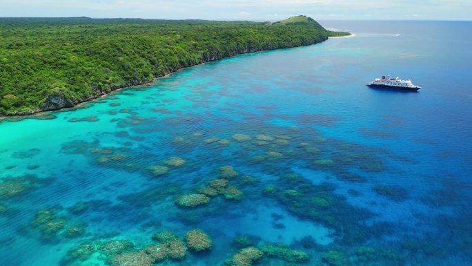 一架无人机在斐济的珊瑚礁上向后飞行，一艘游轮停泊在海岸附近。